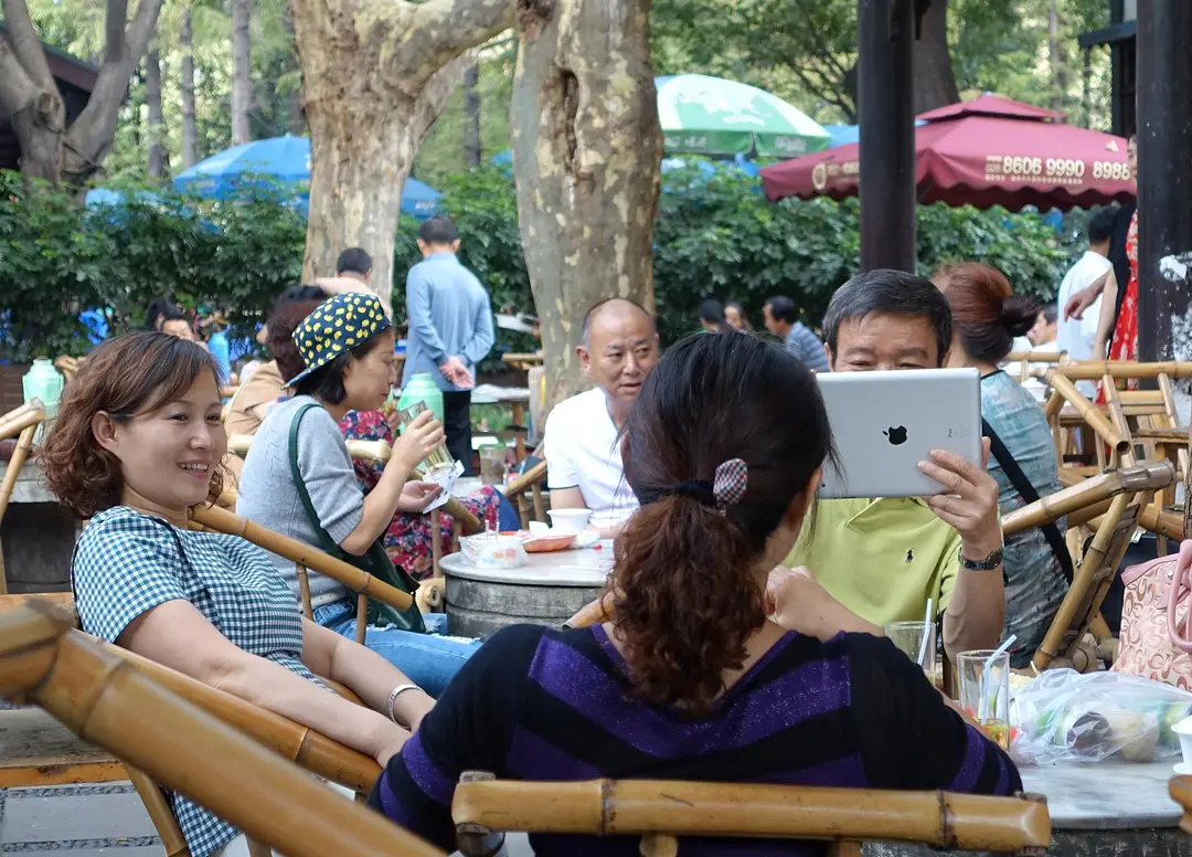 People sitting in bamboo chairs drinking tea and chatting under trees in People's Park