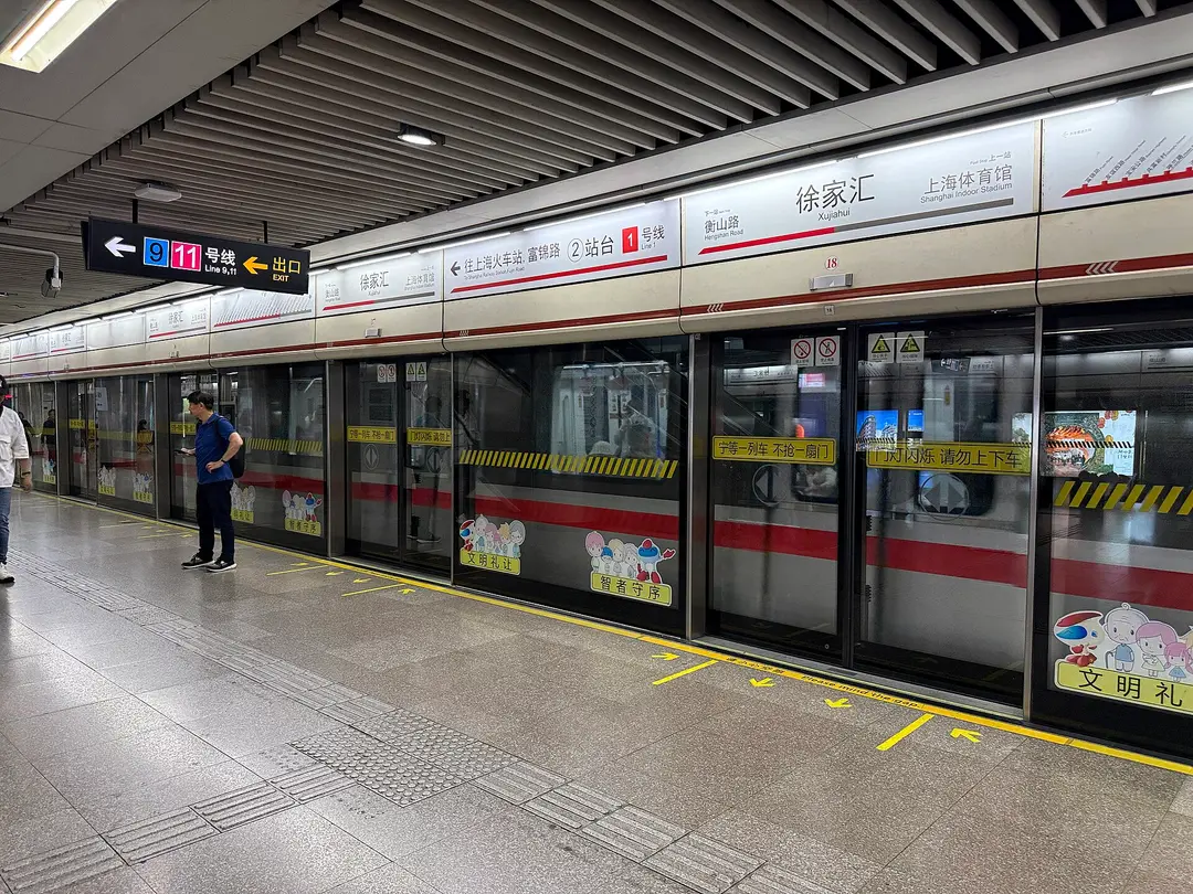 A passenger checking his phone on the Line 1 platform at Xujiahui station, Shanghai, with bilingual signs above