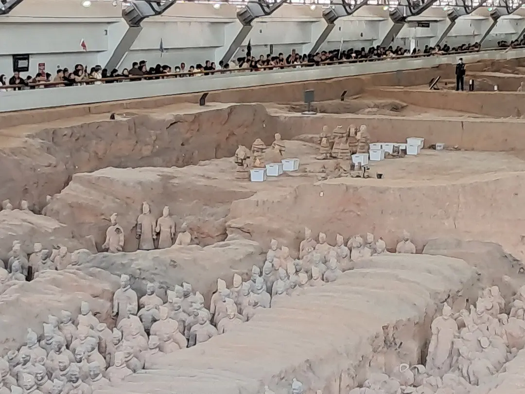 Partly excavated terracotta figures in an earth pit, with visitors watching from the railing above