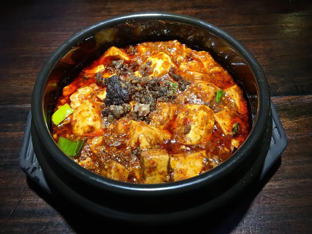 Mapo tofu in red chili sauce with minced meat and spring onion, served in a black stone bowl