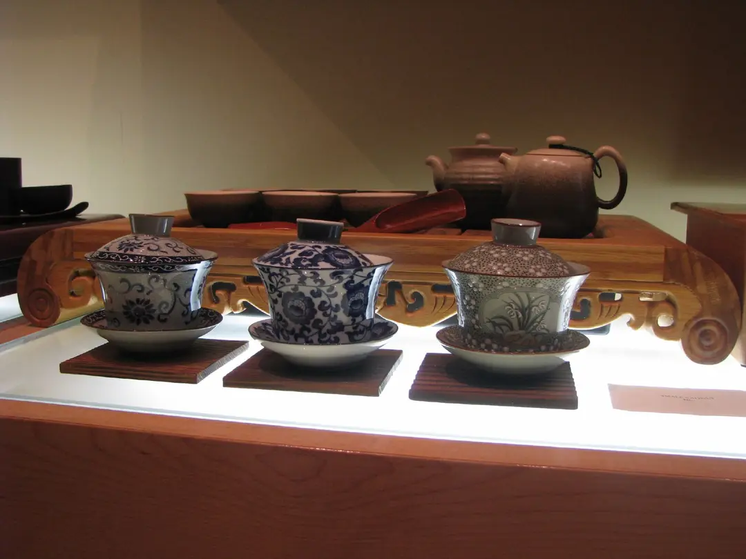 Three porcelain gaiwan tea cups and a clay teapot on a wooden tea tray
