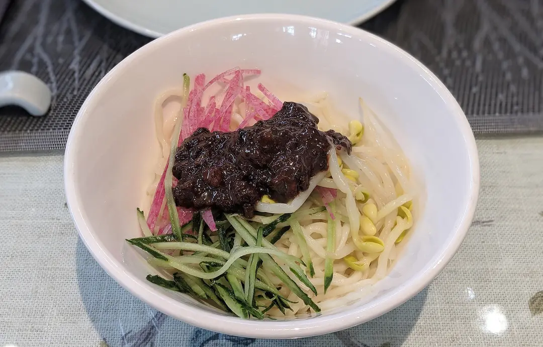 A bowl of zhajiangmian noodles topped with dark bean sauce, cucumber, radish and bean sprouts