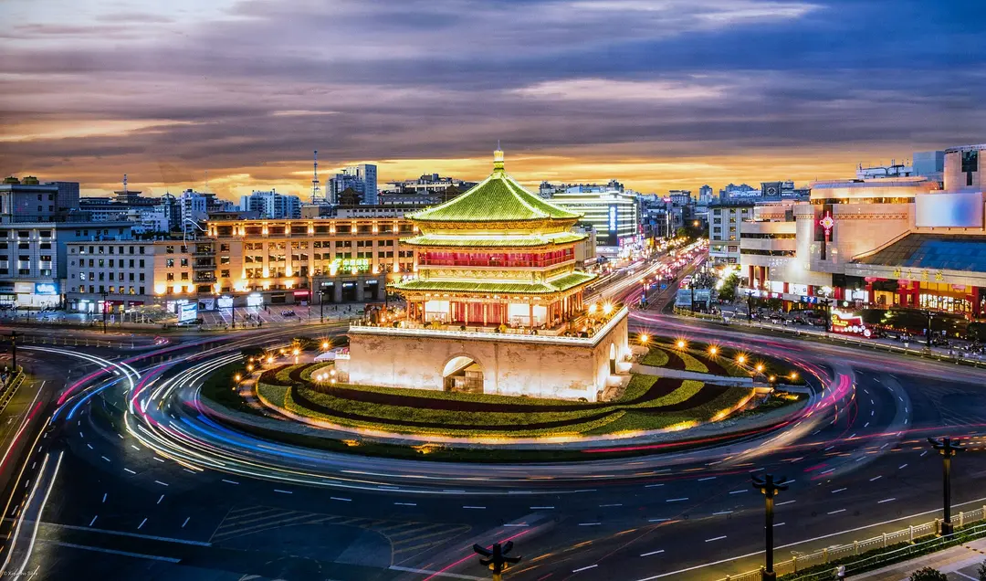The Bell Tower lit up at dusk in the middle of a traffic circle, with light trails from cars around it
