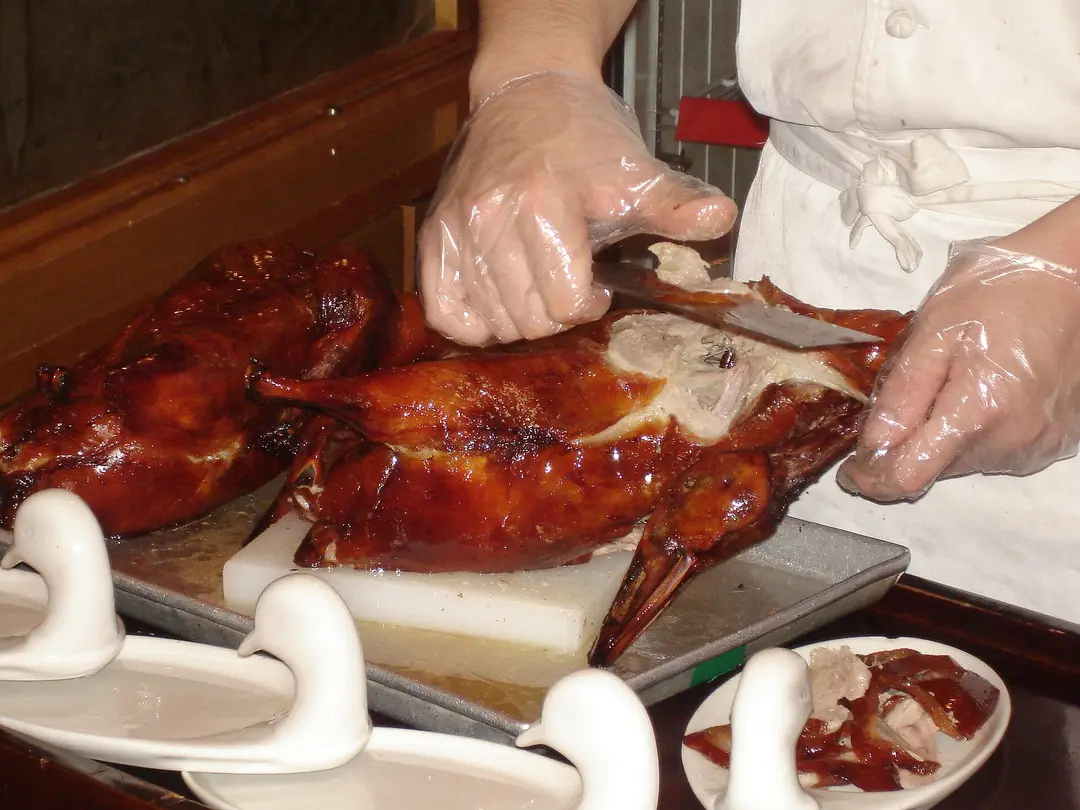 A chef in gloves carving a glossy roast Peking duck at the table