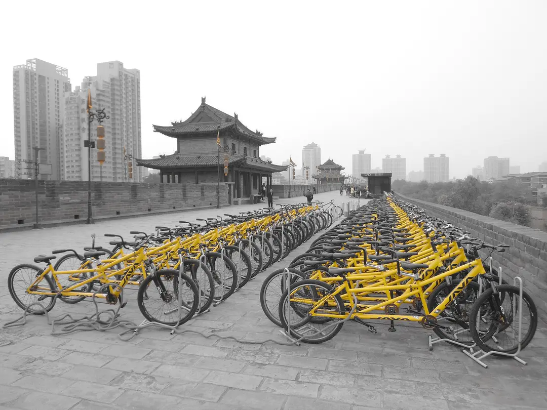 Rows of yellow hire bikes on top of the city wall, with a gate tower and tall buildings behind